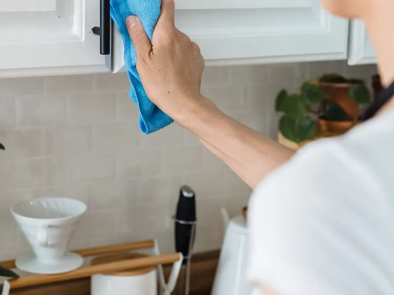 A person wiping a white kitchen cabinet with a blue cloth